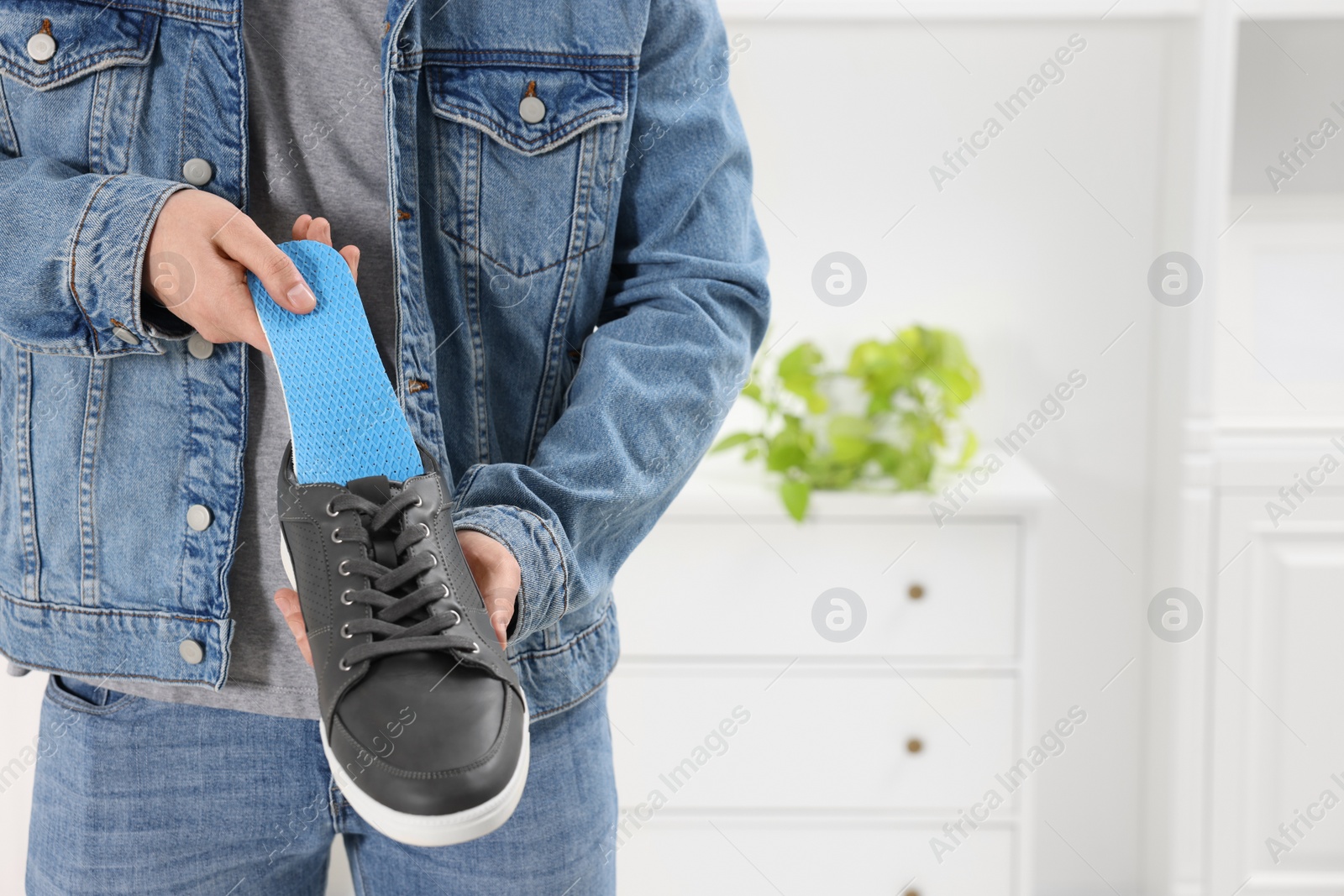 Photo of Man putting orthopedic insole into shoe indoors, closeup. Space for text