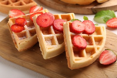 Photo of Tasty Belgian waffles with strawberries and powdered sugar on white table, closeup
