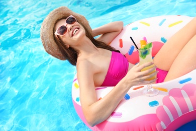 Photo of Young woman with cocktail in pool on sunny day