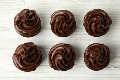 Photo of Delicious chocolate cupcakes with cream on white wooden table, flat lay