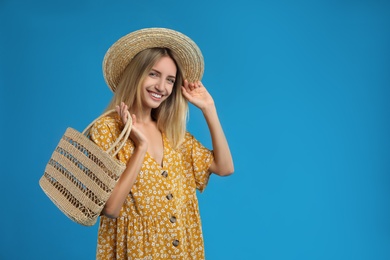 Photo of Beautiful young woman with stylish straw bag on blue background. Space for text