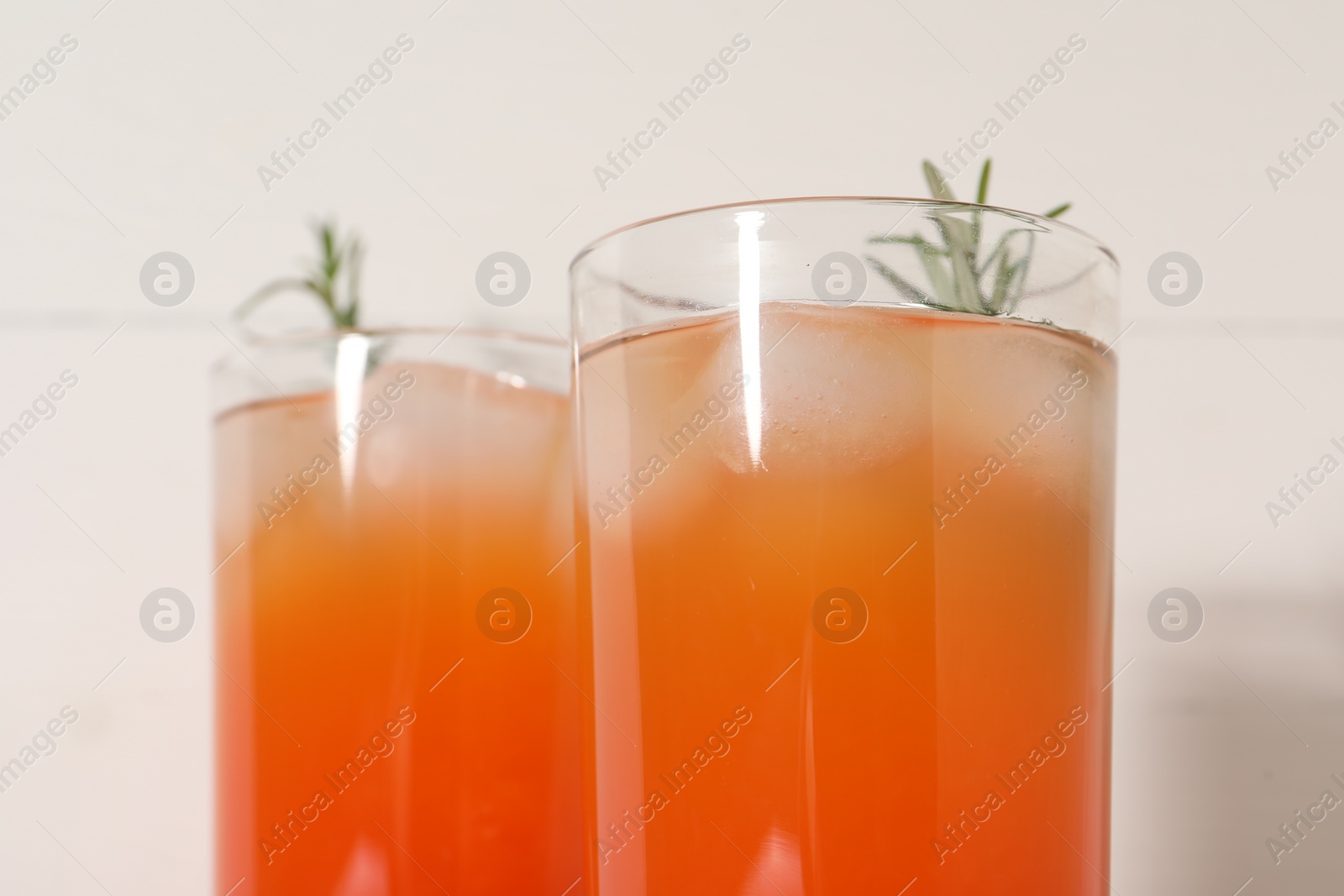 Photo of Tasty grapefruit drink with ice and rosemary in glasses on white background, closeup