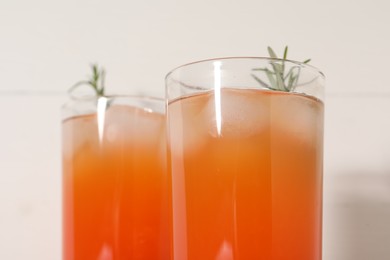 Photo of Tasty grapefruit drink with ice and rosemary in glasses on white background, closeup
