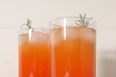 Tasty grapefruit drink with ice and rosemary in glasses on white background, closeup