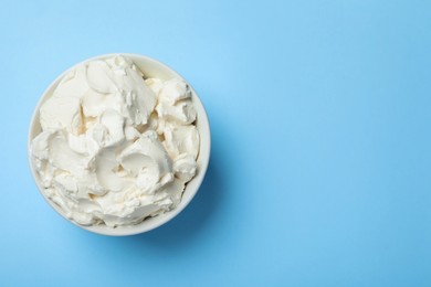 Photo of Bowl of tasty cream cheese on light blue background, top view. Space for text