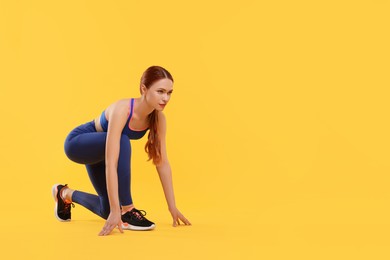 Photo of Young woman in sportswear getting ready to run on yellow background, space for text