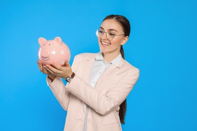 Photo of Happy young businesswoman with piggy bank on light blue background