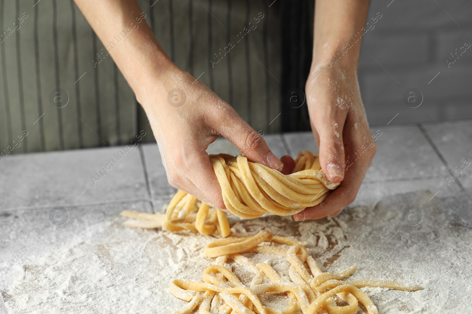 Photo of Woman with homemade pasta at light tiled table, closeup