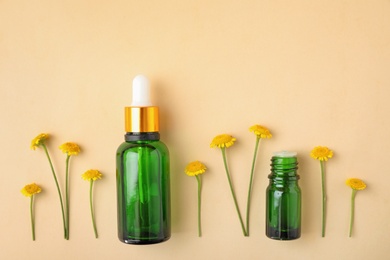 Bottles of essential oil and flowers on color background, flat lay