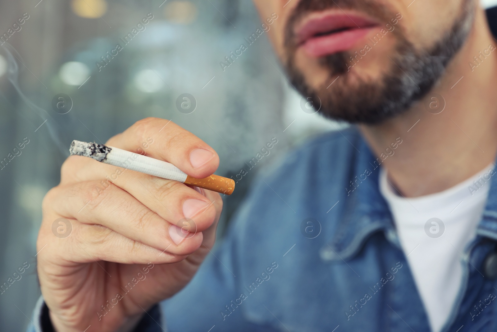 Photo of Handsome man smoking cigarette outdoors, closeup. Bad habit