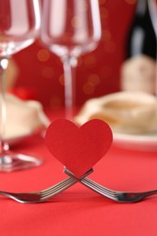 Photo of Joined forks with paper heart on red table, closeup. Romantic dinner