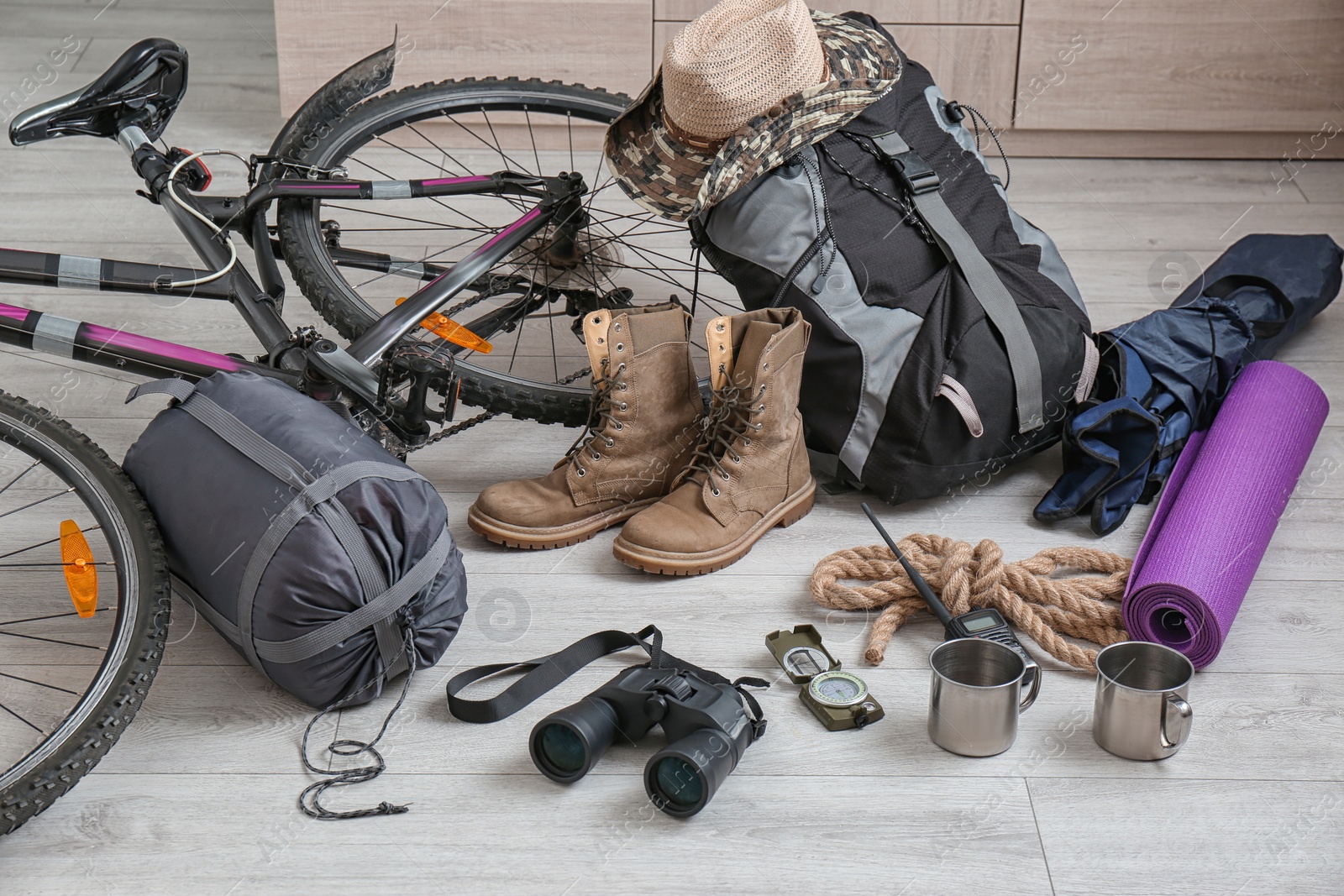 Photo of Sleeping bag, bicycle and set of camping equipment on wooden floor