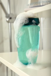 Photo of Bottle of hair care cosmetic product with foam on white shelf indoors