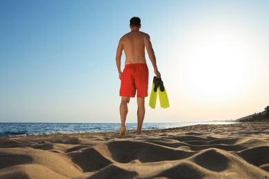 Man with flippers walking along sandy beach, back view