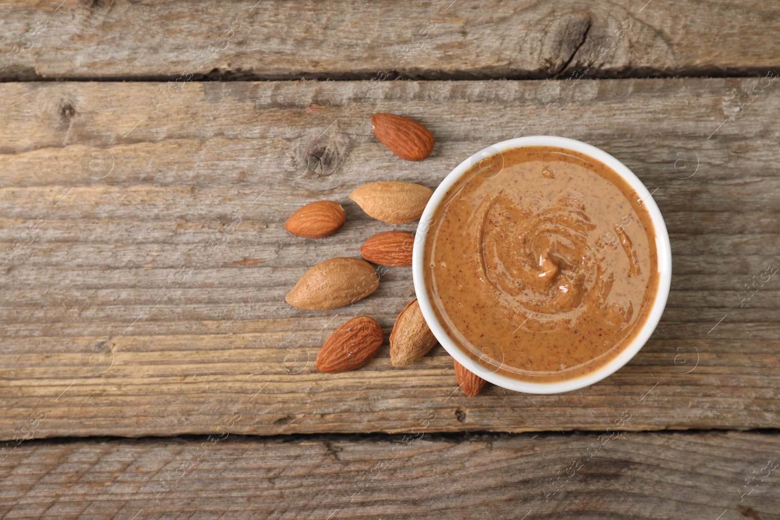 Photo of Delicious nut butter in bowl and almonds on wooden table, top view. Space for text