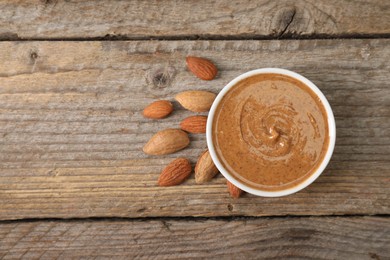 Delicious nut butter in bowl and almonds on wooden table, top view. Space for text