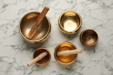 Golden singing bowls with mallets on white marble table, flat lay