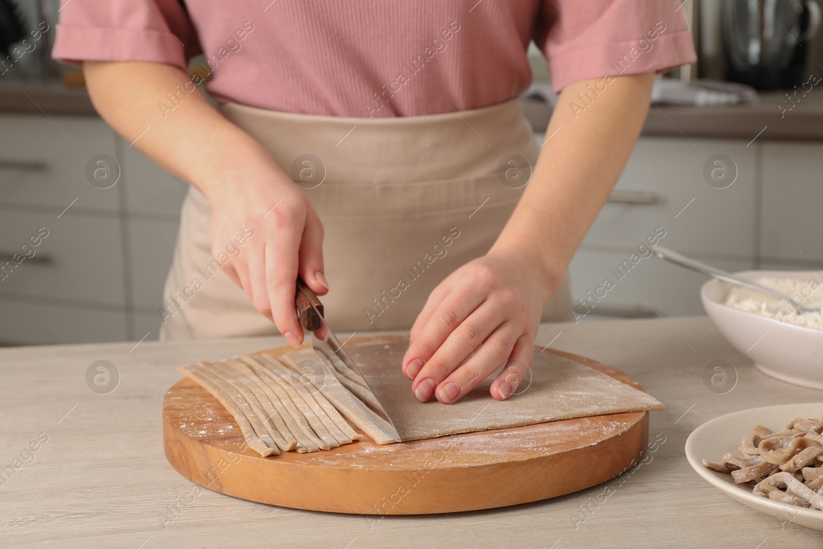 Photo of Woman making soba (buckwheat noodles) at wooden table in kitchen, closeup