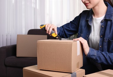 Young woman using utility knife to open parcel at home, closeup