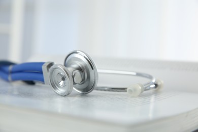 Photo of One medical stethoscope and book on table, closeup