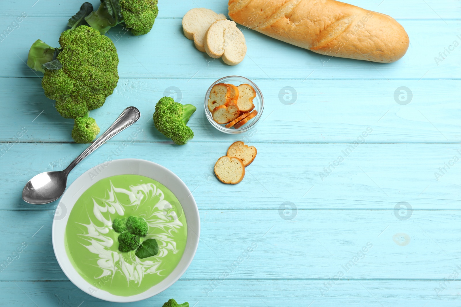 Photo of Flat lay composition with bowl of cheese cream soup and broccoli on blue wooden table. Space for text