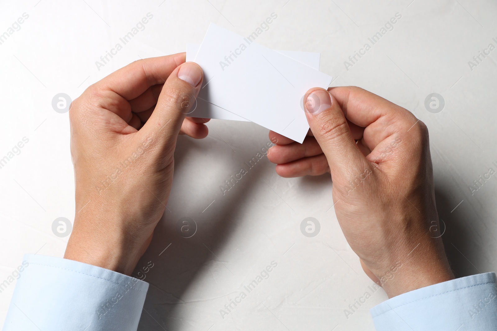 Photo of Man holding blank cards at white table, top view. Mockup for design