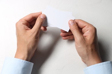 Man holding blank cards at white table, top view. Mockup for design