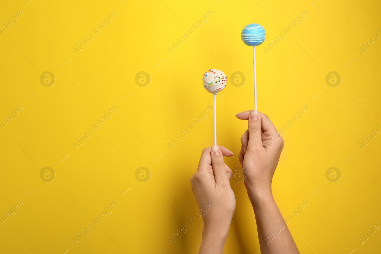 Photo of Woman holding bright delicious cake pops on color background, closeup. Space for text