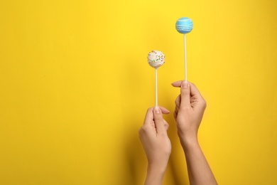 Woman holding bright delicious cake pops on color background, closeup. Space for text