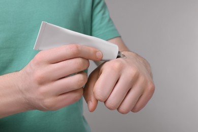 Photo of Man applying ointment from tube onto hand on light grey background, closeup