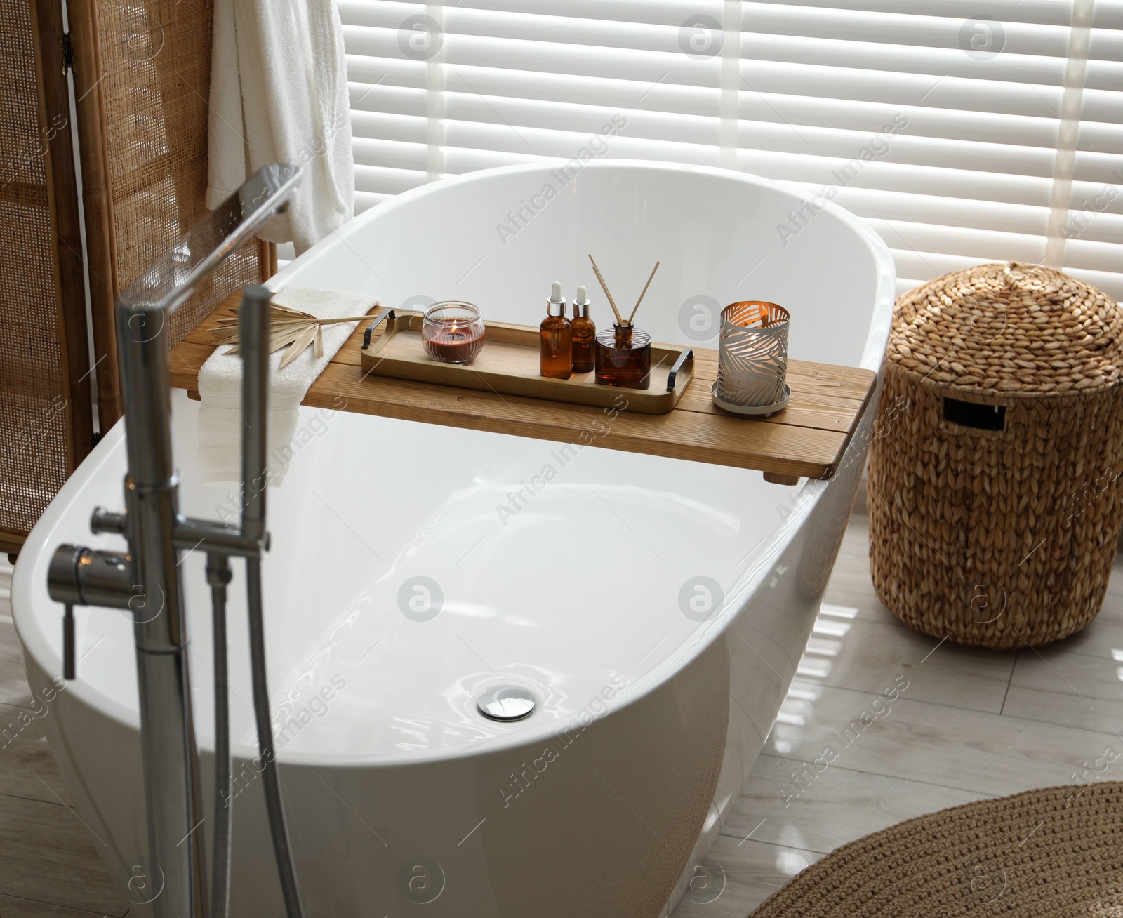 Photo of Wooden tray with cosmetic products, burning candles, and reed air freshener on bath tub in bathroom