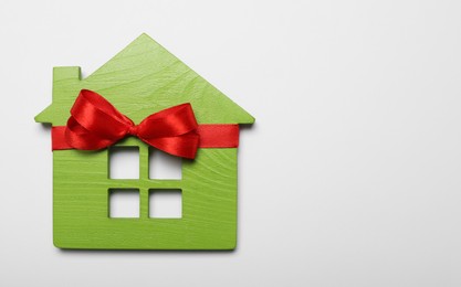 Wooden house model with red bow on white background, top view. Housewarming party