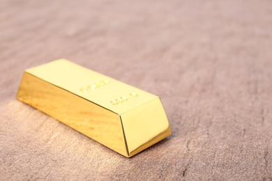 Photo of Shiny gold bar on table, closeup. Space for text