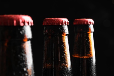 Photo of Bottles of tasty cold beer on black background, closeup