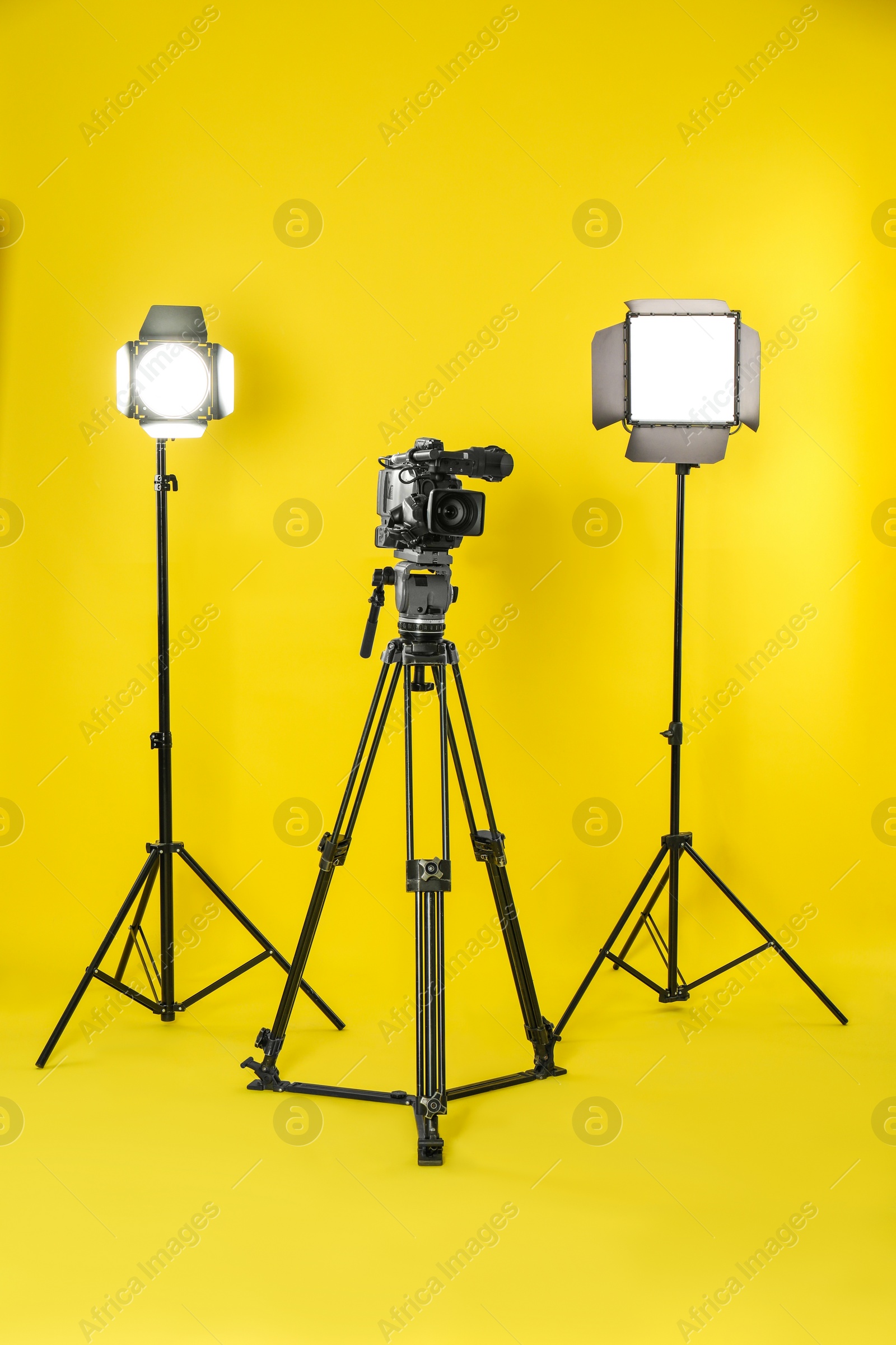 Photo of Professional video camera and lighting equipment on yellow background