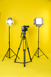 Photo of Professional video camera and lighting equipment on yellow background