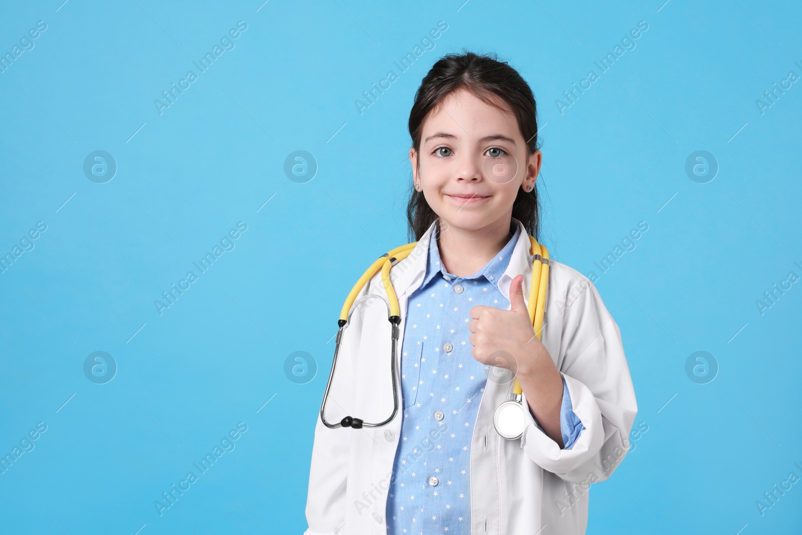 Photo of Little girl with stethoscope dressed as doctor on light blue background, space for text. Pediatrician practice