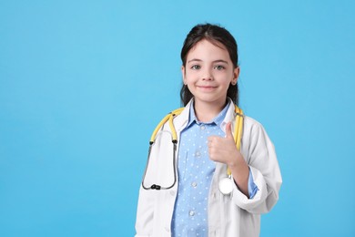 Little girl with stethoscope dressed as doctor on light blue background, space for text. Pediatrician practice