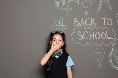 Little child in uniform near drawings with text BACK TO SCHOOL on grey background