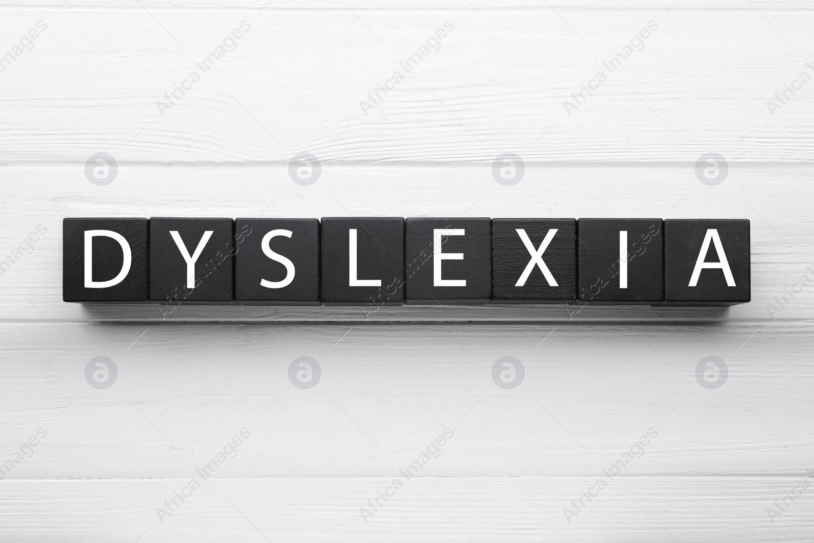 Photo of Black cubes with word Dyslexia on white wooden background, flat lay