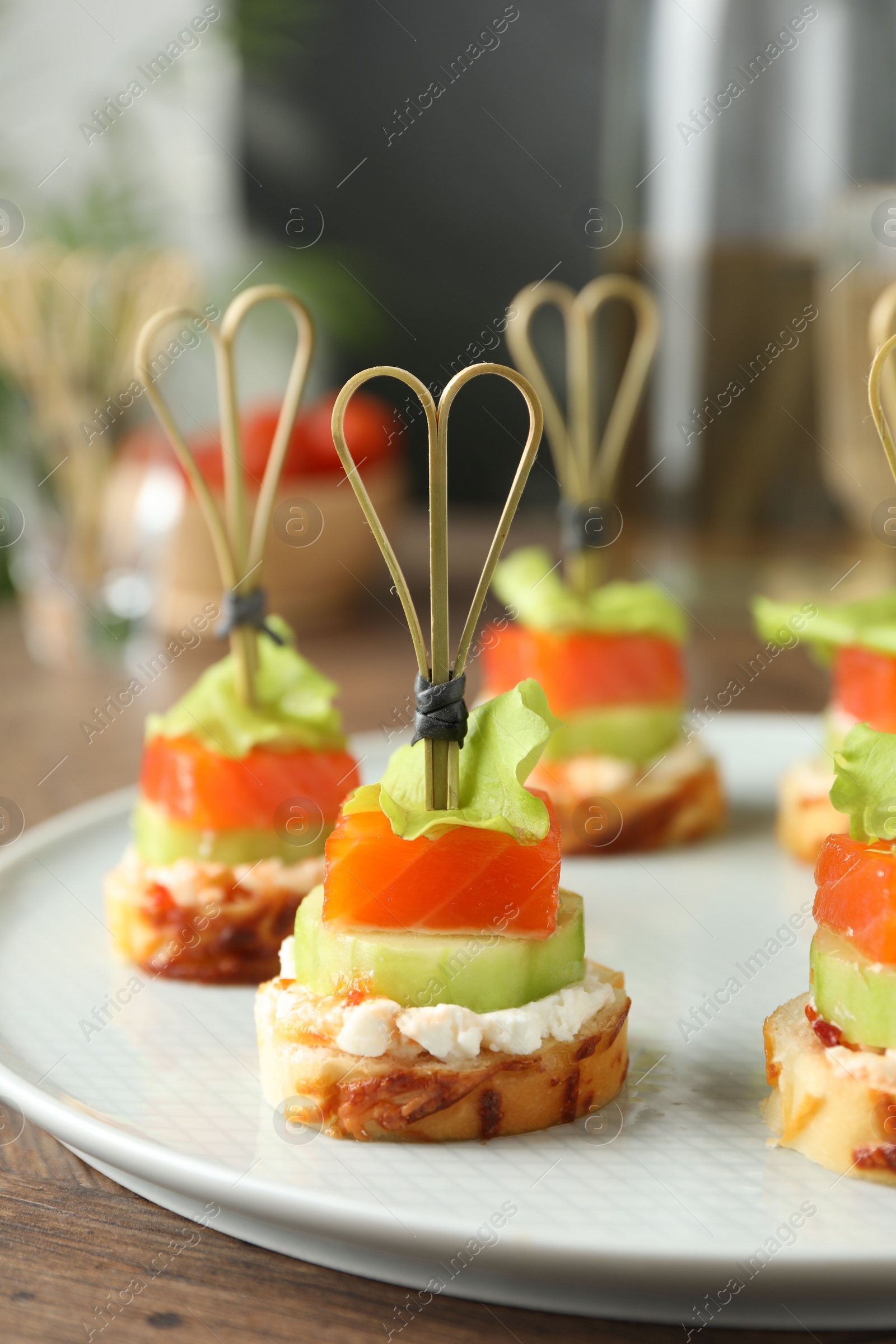 Photo of Tasty canapes with salmon, cucumber, bread and cream cheese on wooden table, closeup