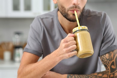 Photo of Man drinking delicious smoothie in kitchen, closeup