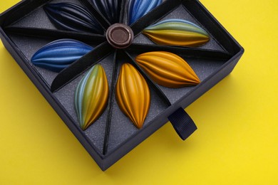 Photo of Box of tasty chocolate candies on yellow background, above view