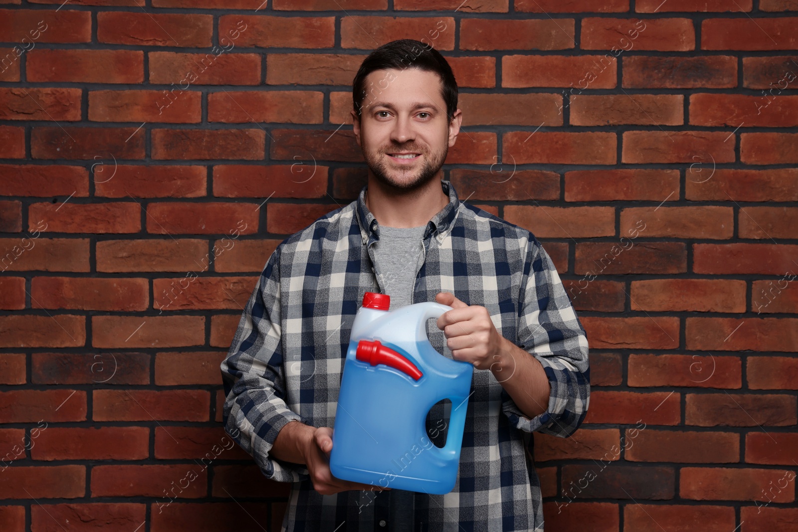 Photo of Handsome man holding canister with blue liquid near brick wall