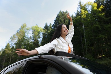Enjoying trip. Happy woman leaning out of car roof outdoors