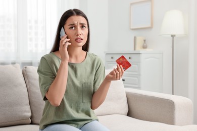 Confused woman with credit card talking on phone at home. Be careful - fraud