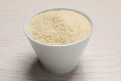 Photo of Delicious grated parmesan cheese in bowl on white wooden table
