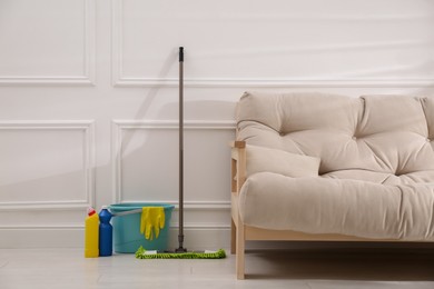 Photo of Floor mop, cleaning detergents and bucket with gloves near white wall in living room