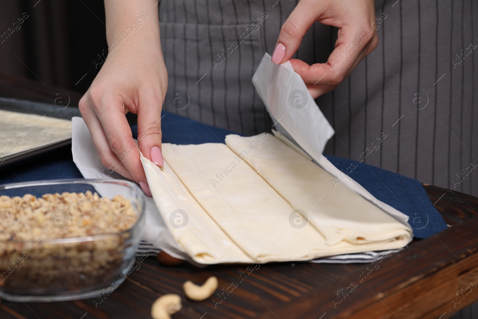 Photo of Making delicious baklava. Woman with dough at wooden table, closeup