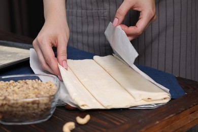 Photo of Making delicious baklava. Woman with dough at wooden table, closeup